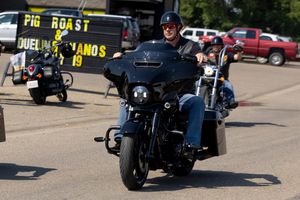 Classic antique black automobiles line up in a row at a vintage car show during a sunny outdoor event.