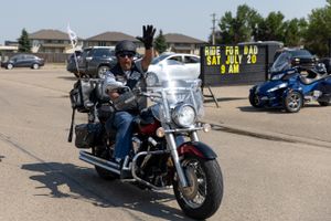 A motorcyclist waves while riding past a sign that reads 'The Old Man Can Still Ride'.