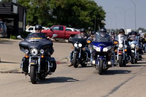 A group of motorcycles riding in formation on a road, led by black and blue bikes.
