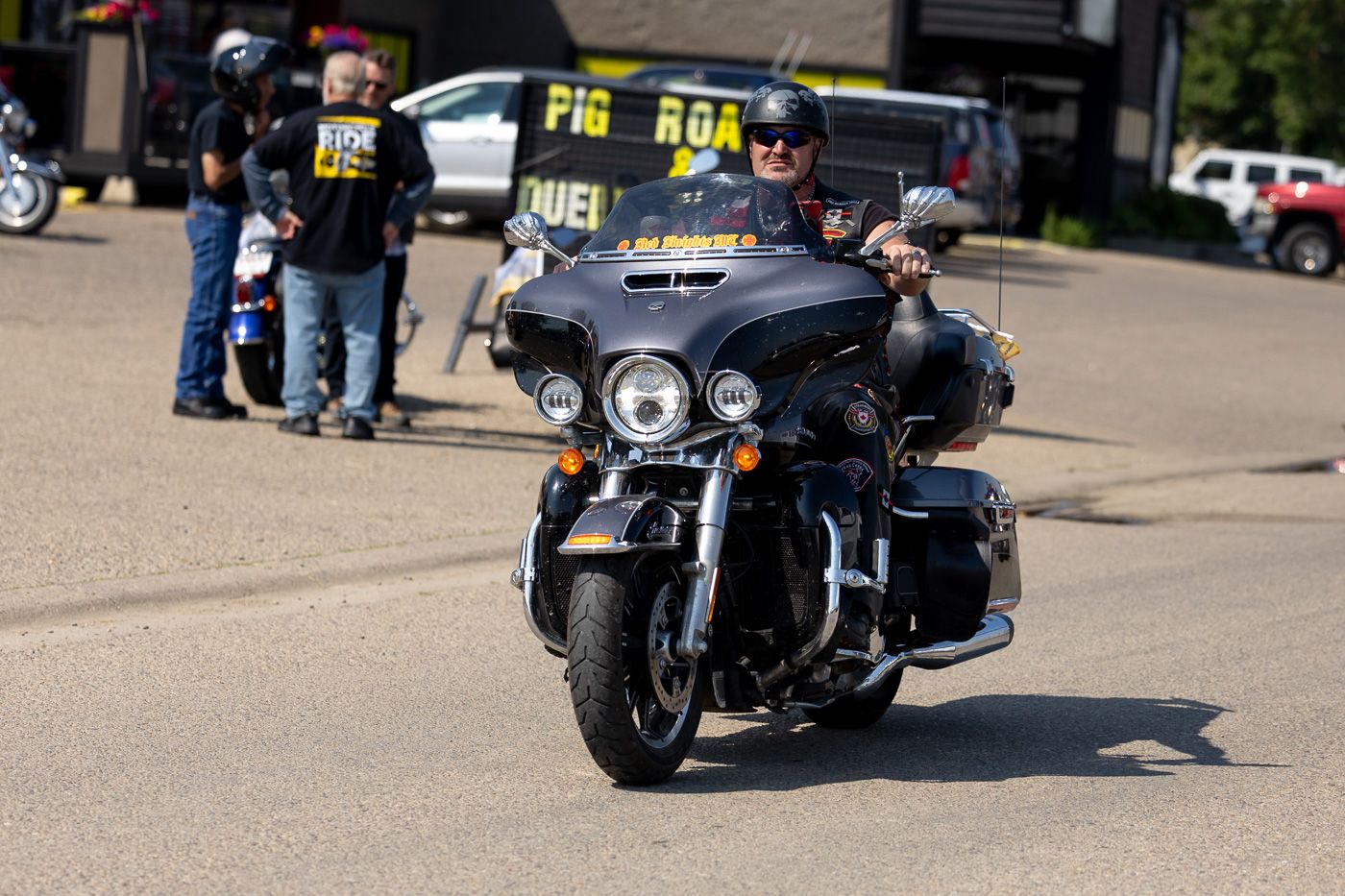 A line of parked black Harley Davidson motorcycles arranged in a row on a sunny outdoor parking lot.