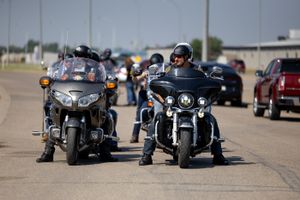 Motorcyclists riding large touring bikes on a road with cars in the background.