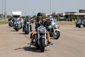 A row of parked motorcycles lined up at a motorcycle rally showing chrome and custom details in bright sunlight.