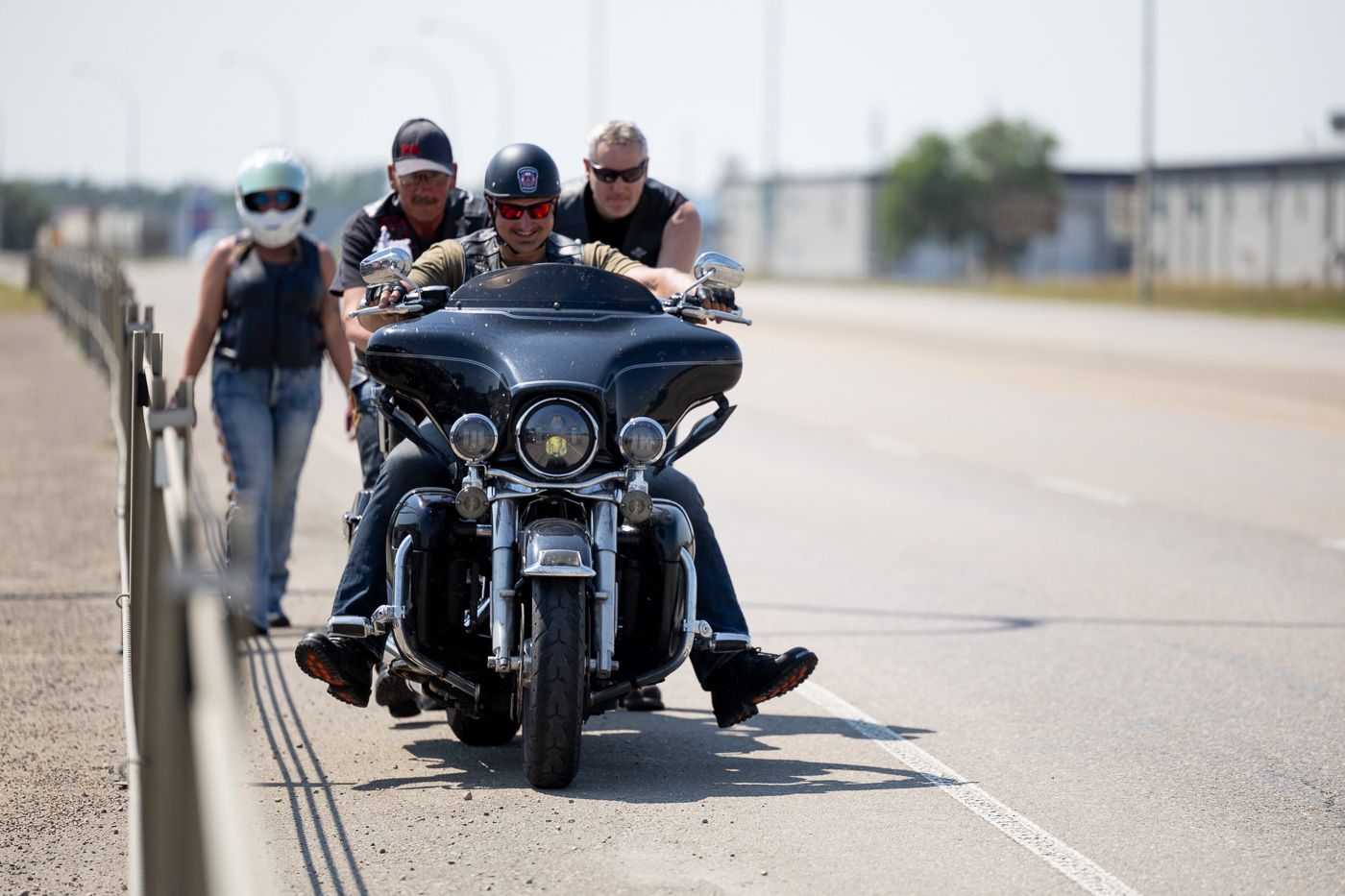 Motorcyclists ride in a line on a highway, with the lead bike carrying multiple passengers.
