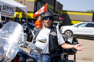 Motorcyclist gesturing enthusiastically next to parked bikes at an outdoor gathering.
