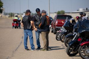 Three motorcyclists in leather jackets conversing next to parked motorcycles.