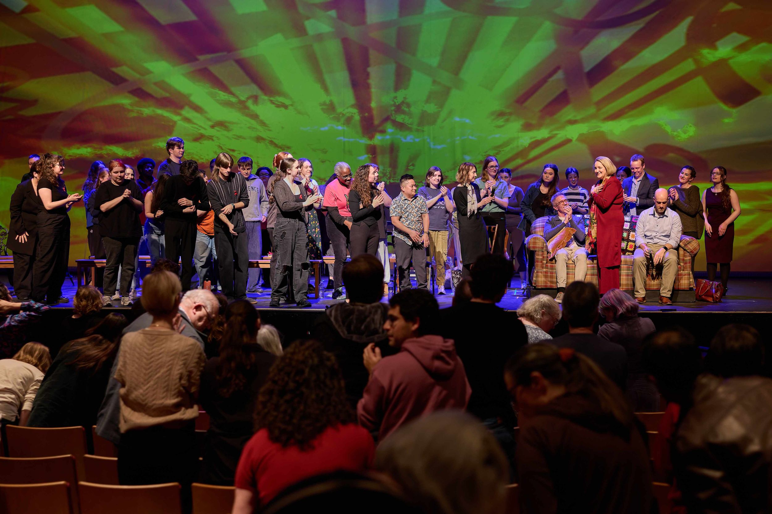 The crowd on stage and in the theater's house give a standing ovation to a woman as she enters the stage.