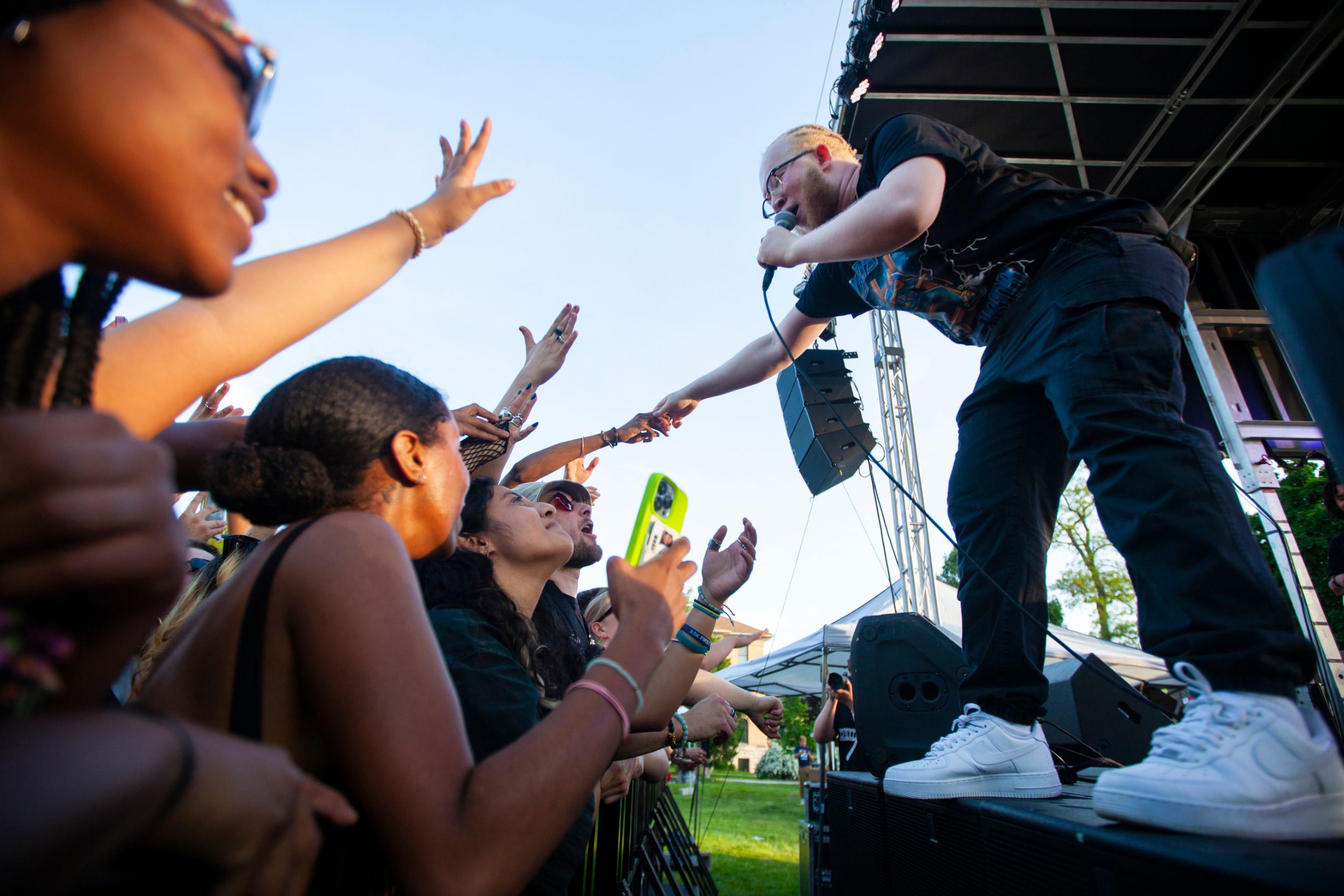 A musician shakes hands with the crowd at a festival from the stage.