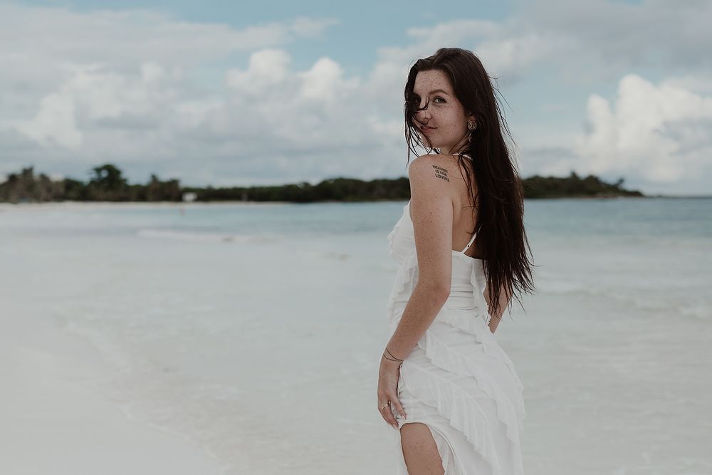 Editorial engagement portrait of a woman in a white dress by the sea in Riviera Maya.