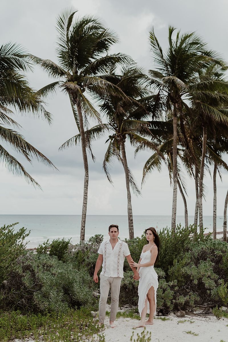 Couple standing together under palm trees during a destination engagement photoshoot in Mexico.