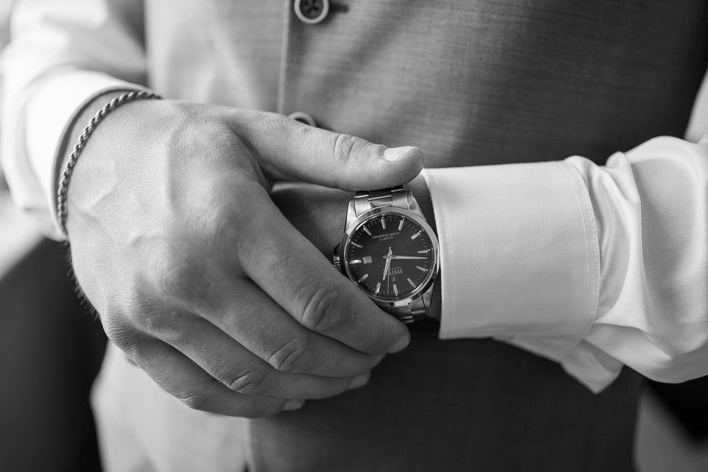 Close-up view of hands adjusting a wristwatch with a dark face and leather strap.
