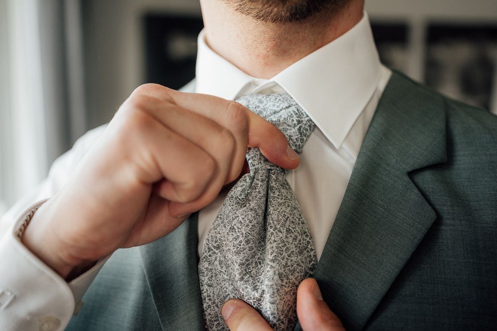 A close-up detail shot of a gray knit tie and dark suit lapel against a white dress shirt.