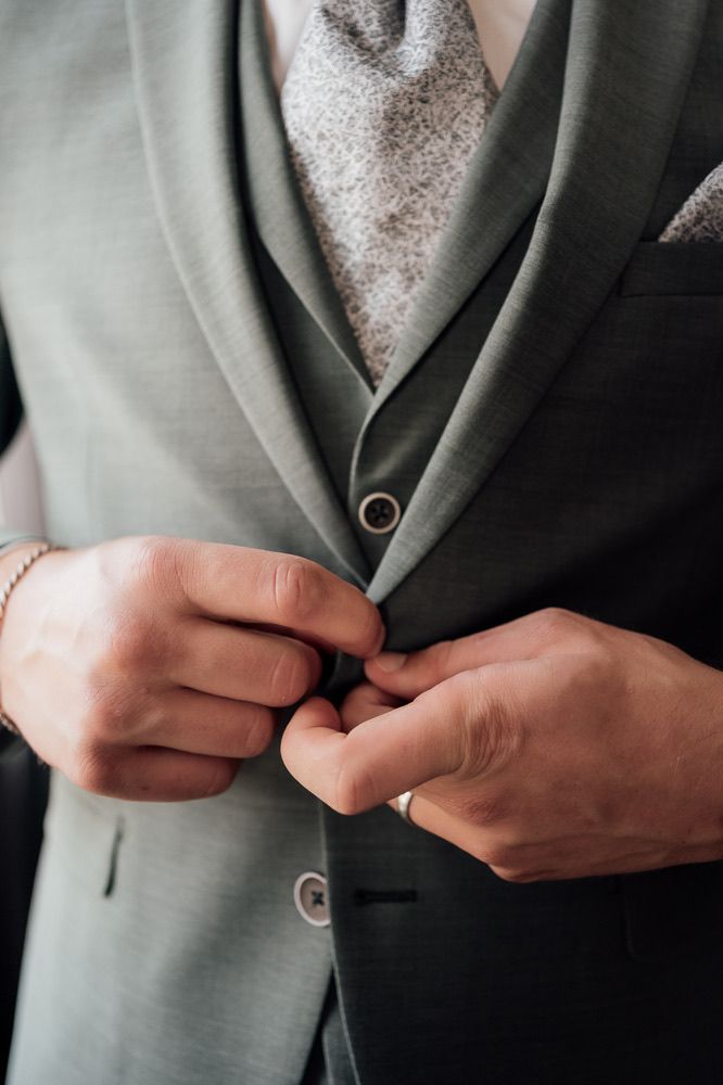 Close-up shots of hands buttoning a light gray suit jacket against a dark background.