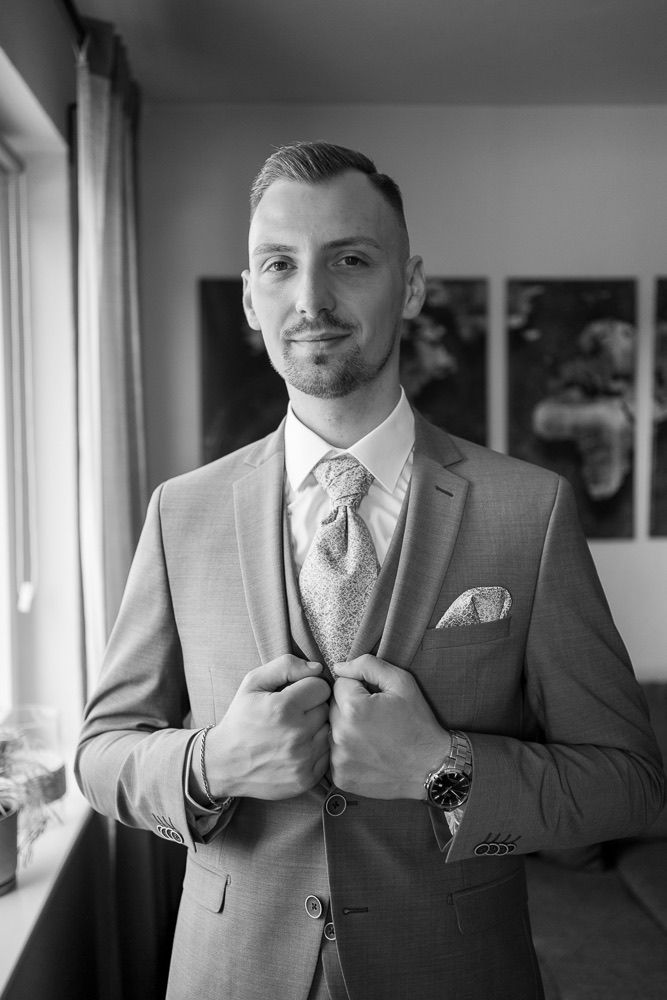 A series of black and white photos showing details of a groom getting ready in a light colored suit and tie.