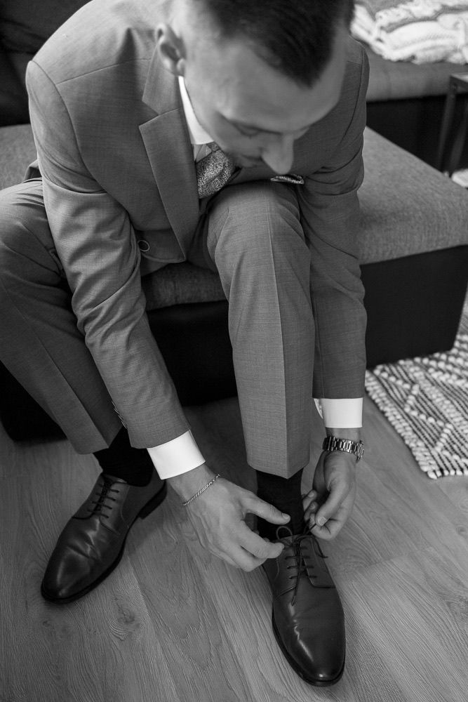 Black and white image sequence showing a person in a suit tying their dress shoes on a wooden floor.