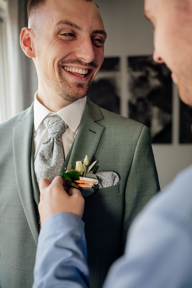 A series of photos showing someone adjusting a boutonniere on a sage green suit jacket with a silver patterned tie.
