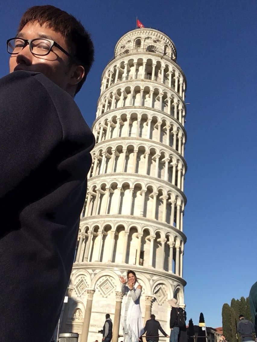 Tourist poses for a creative perspective trick photo with the Leaning Tower of Pisa in Italy under clear blue skies.