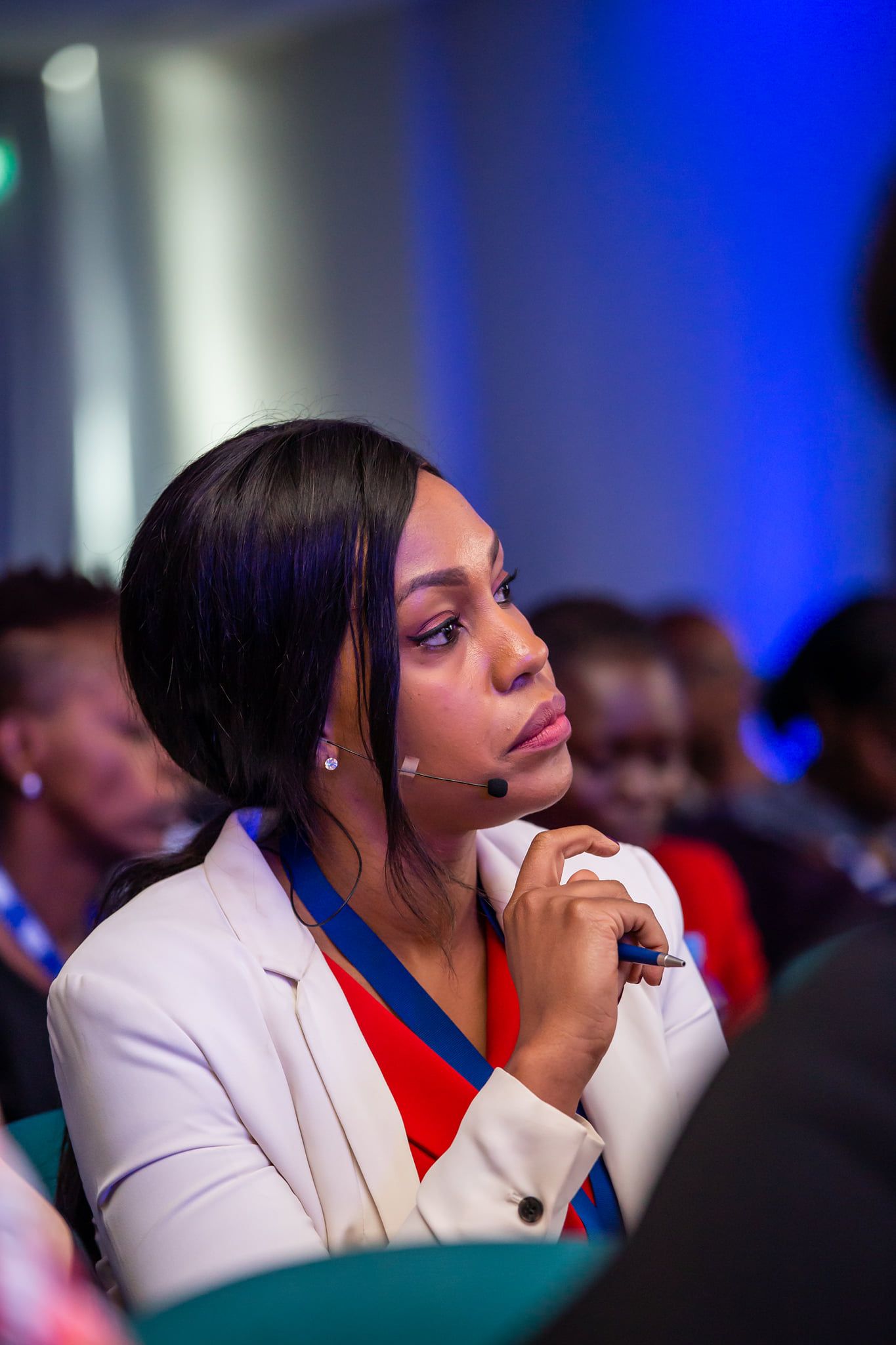 Professional conference attendee in a suit takes notes at a blue-lit event with water bottles on the table.
