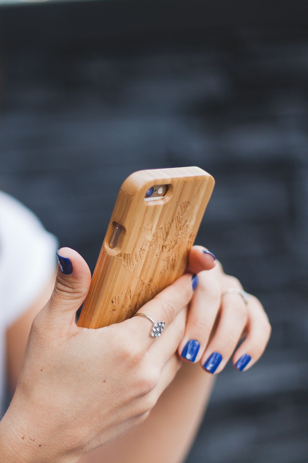 Close-up of hands with blue nails and ring holding engraved bamboo wood iPhone case.