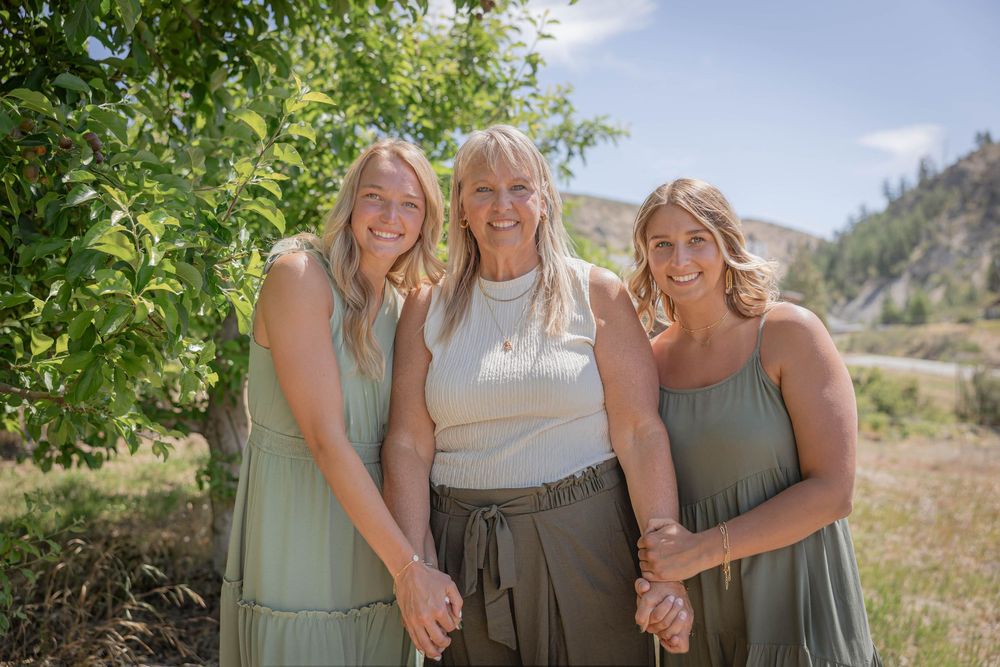 Three people in casual summer attire posing together outdoors with mountains in background.