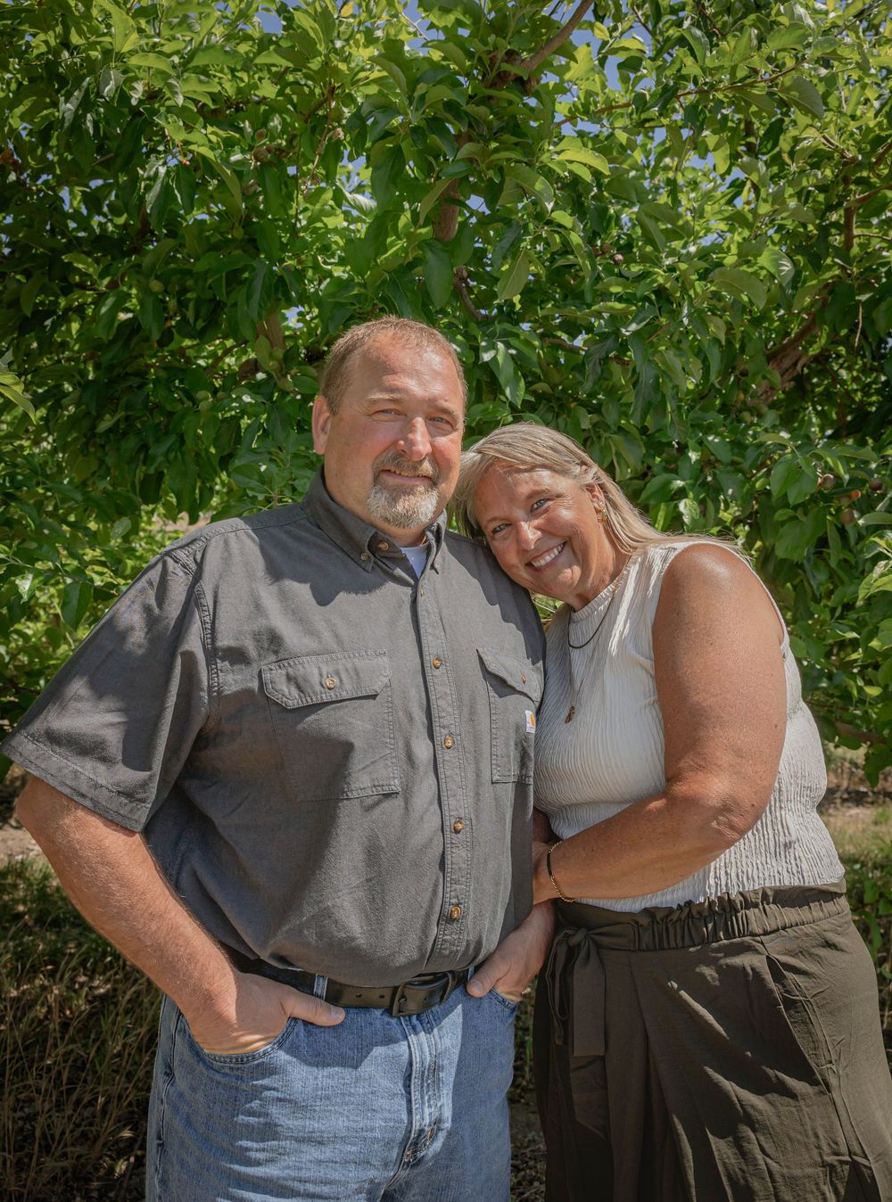 Couple embracing outdoors under green leafy trees on a sunny day.