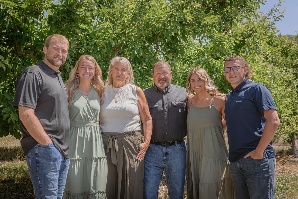 Family members gather for a group photo in front of trees on a sunny afternoon.
