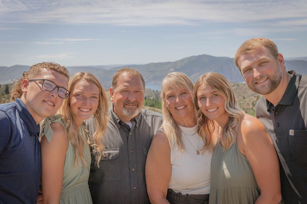 Group photo taken outdoors with mountains and blue sky visible in the background.