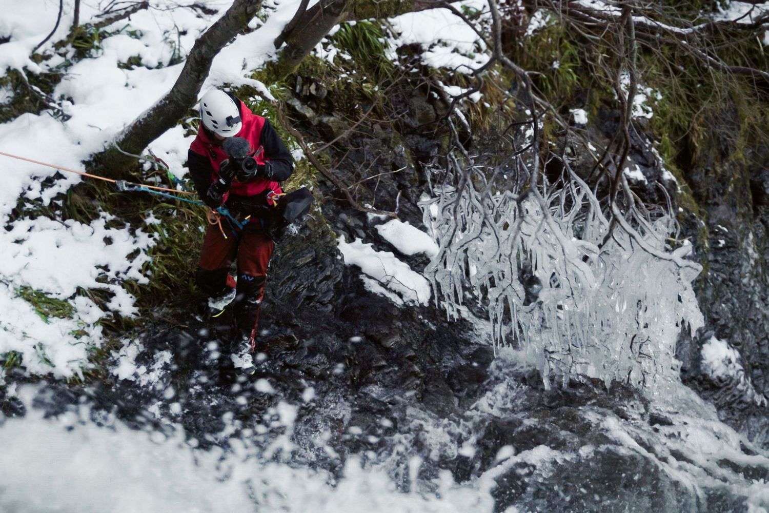 Expedition filmmaker on a rope above a waterfall covered in ice