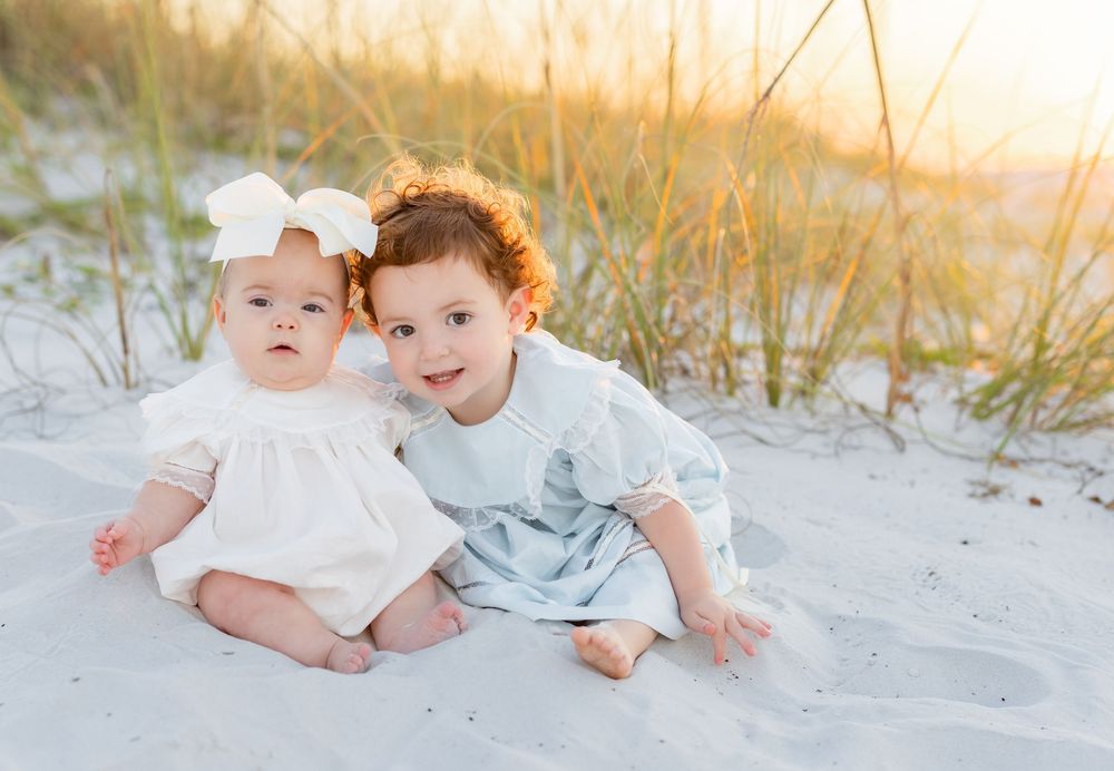 A series of tender lifestyle images of siblings in soft blue and white outfits lying together on a beach at sunset.