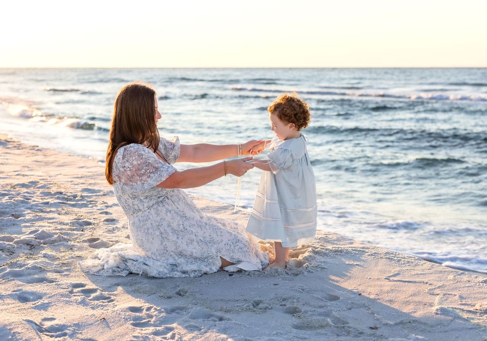 Two people enjoying a tender moment while playing on a white sandy beach at sunset next to the ocean waves.