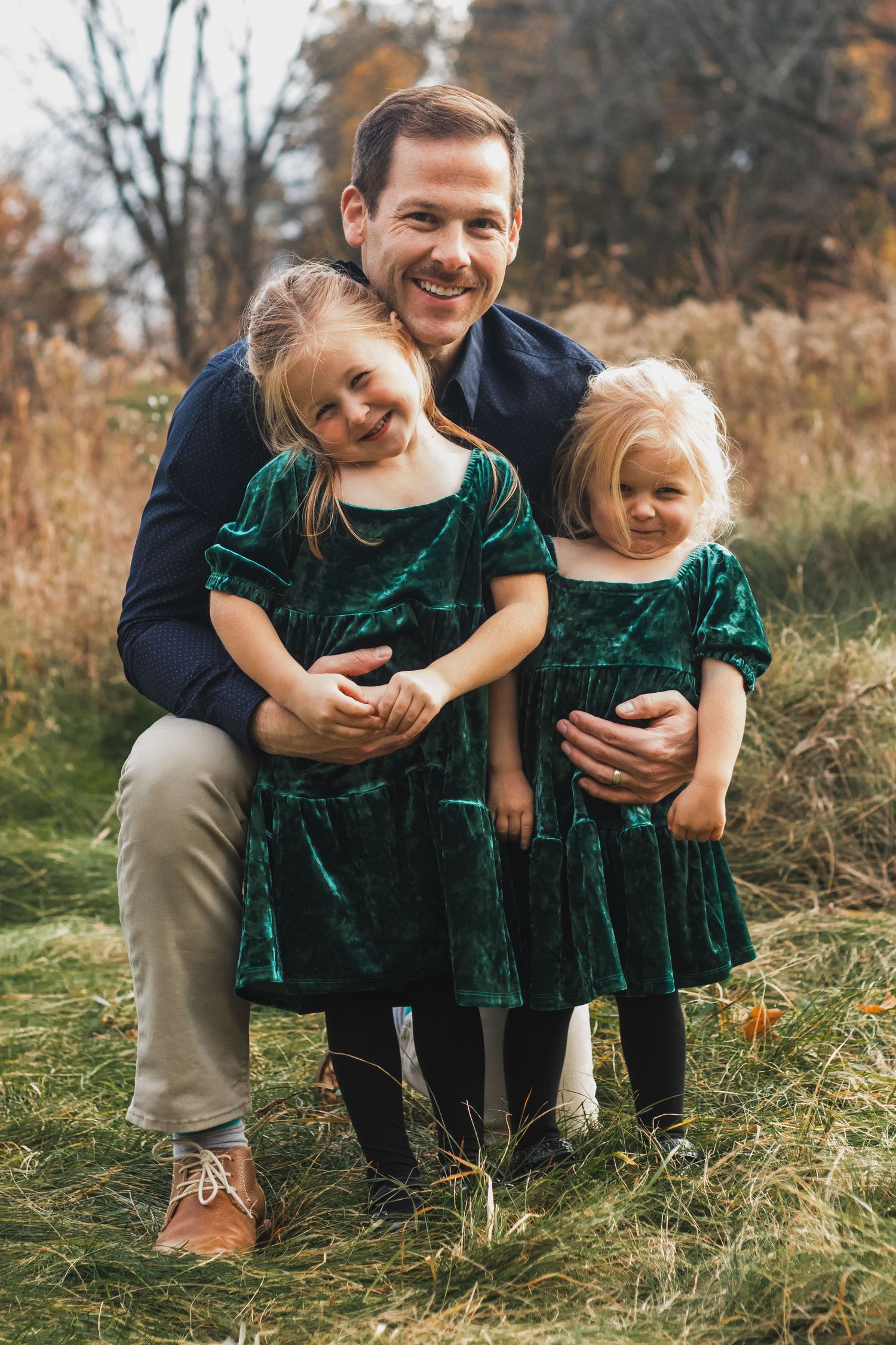 Father keeling with his two daughters smiling during a lifestyle family photography golden hour session in South Lyon, Michigan.