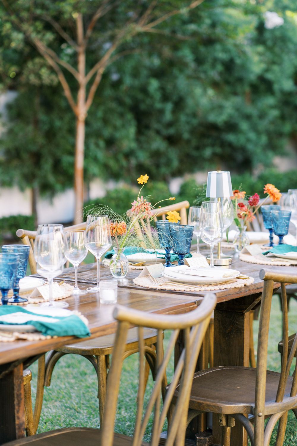 Elegant outdoor dining table setup with wooden chairs and wine glasses in a garden setting.