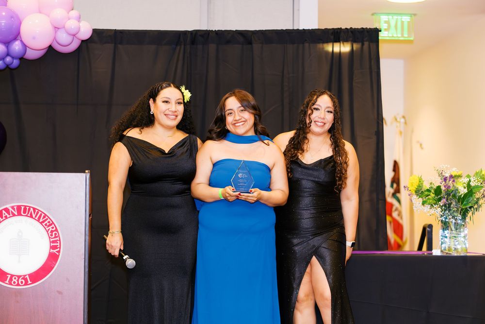 Three women in formal attire standing on stage at an awards ceremony.
