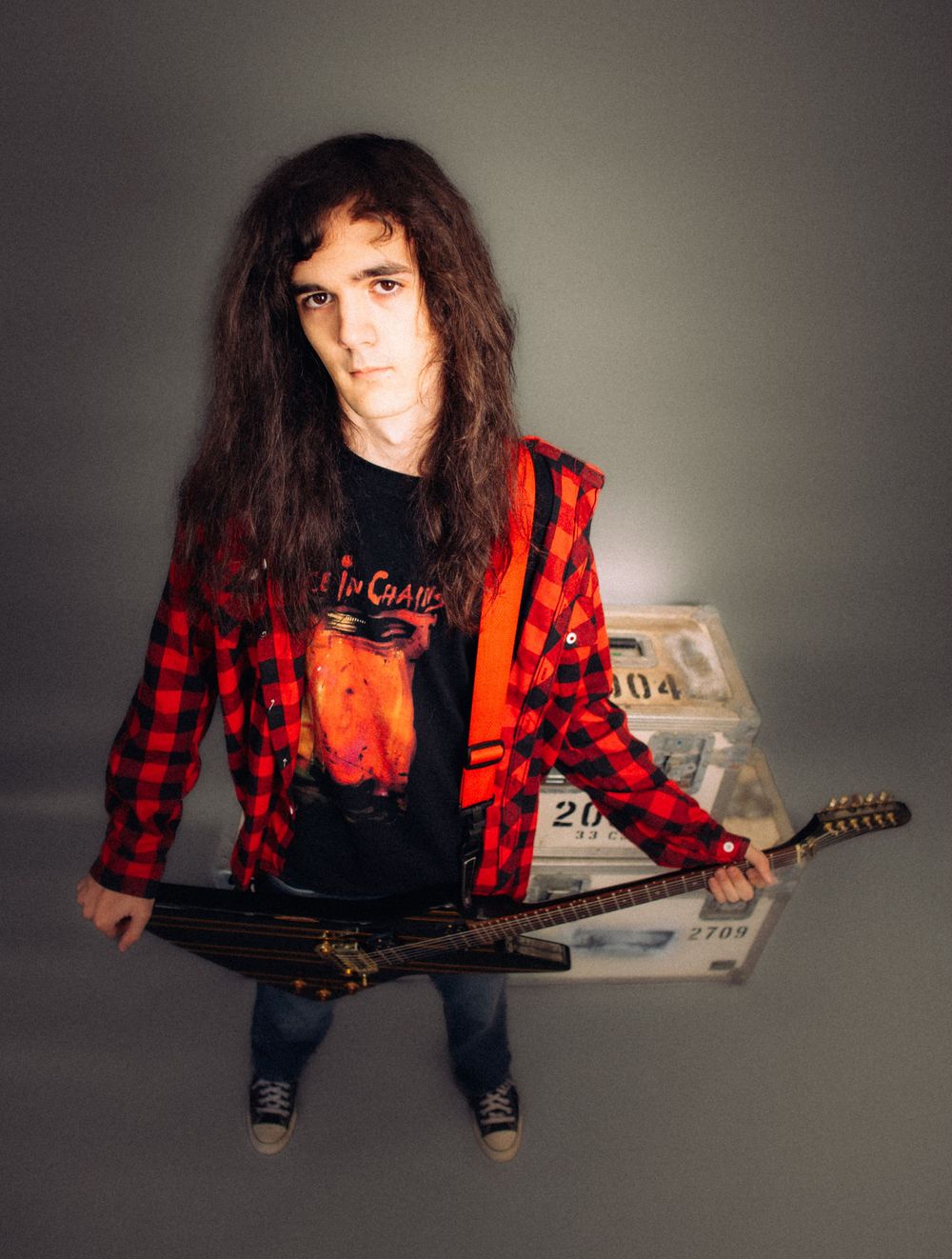 Rock musician with long dark hair holding electric guitar in red flannel shirt with cash stacks.