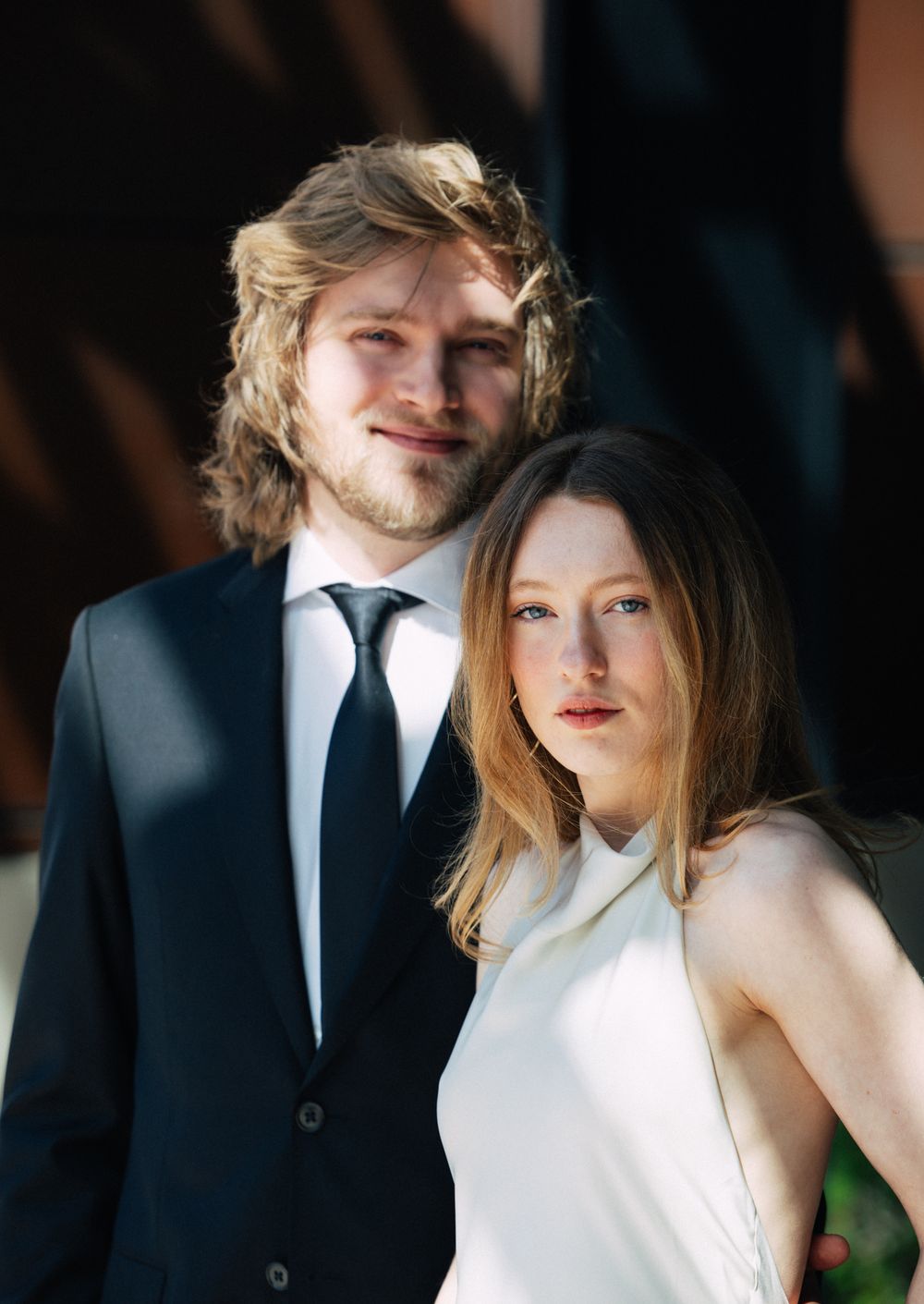 Elegant couple in formal attire posing together, man in black suit with tie and woman in white dress.