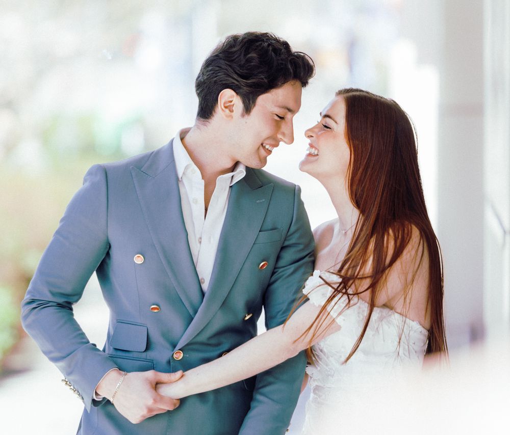 Romantic couple in elegant attire smiling and holding hands in a bright, airy setting.