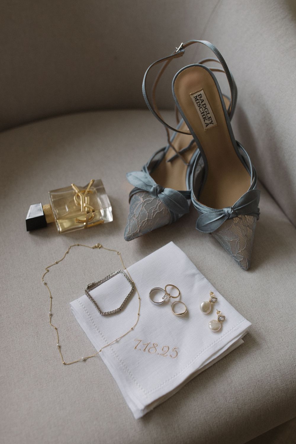 Wedding details including silver heels, rings, and invitations styled on beige surface.