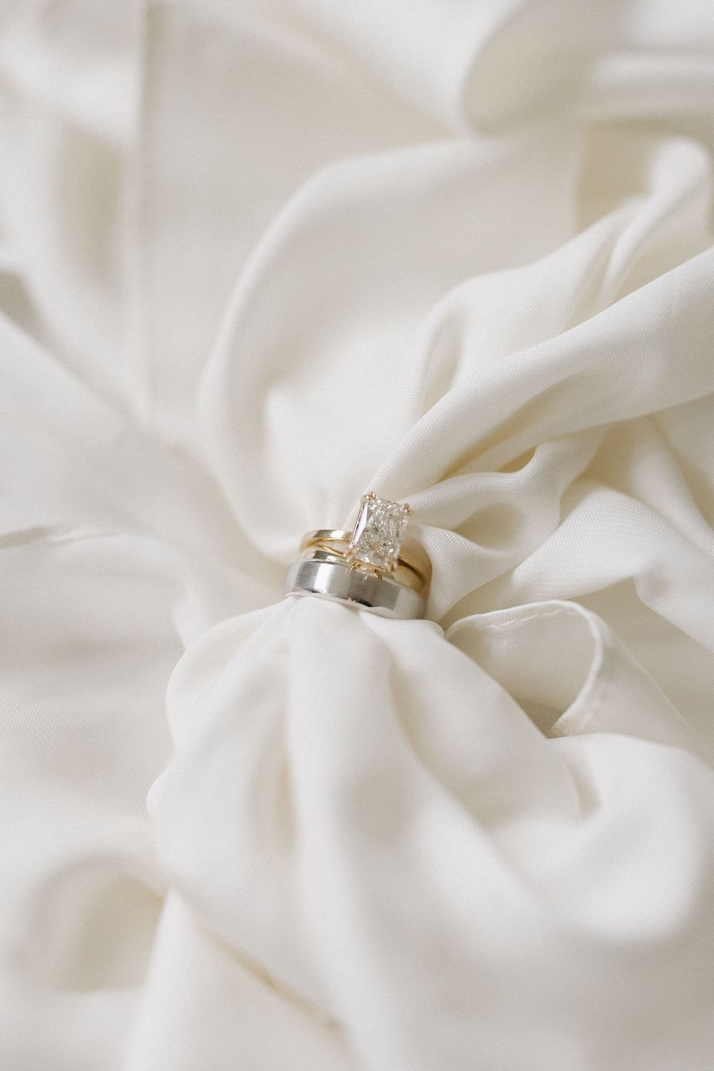 Wedding rings nestled in soft white fabric creating elegant texture and shadows.