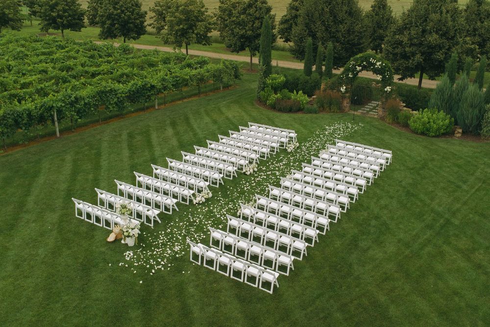 Aerial view of white chairs arranged in rows on a lush green lawn for an outdoor wedding ceremony.