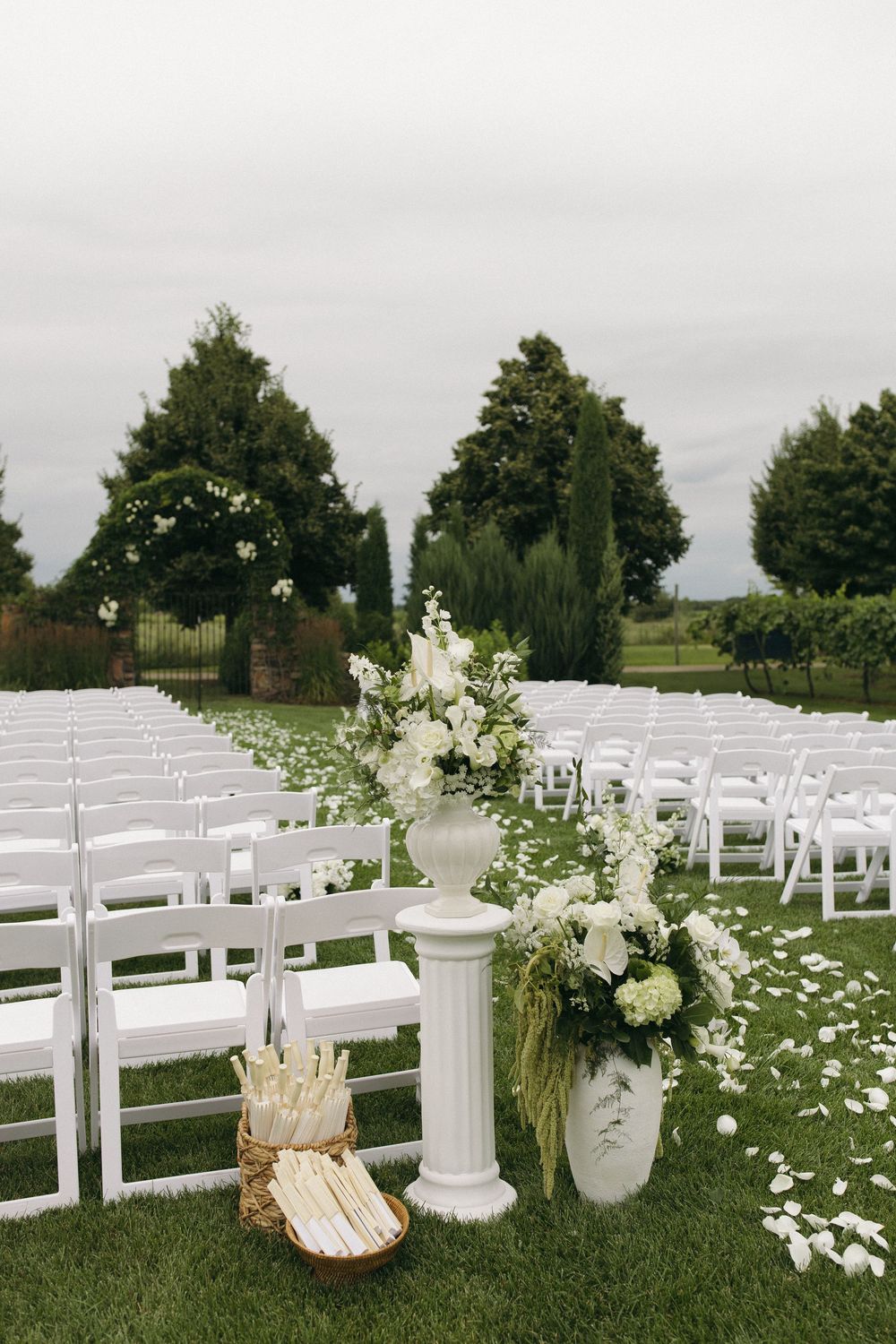 White garden chairs set up for outdoor wedding ceremony with floral arrangements and scattered petals.