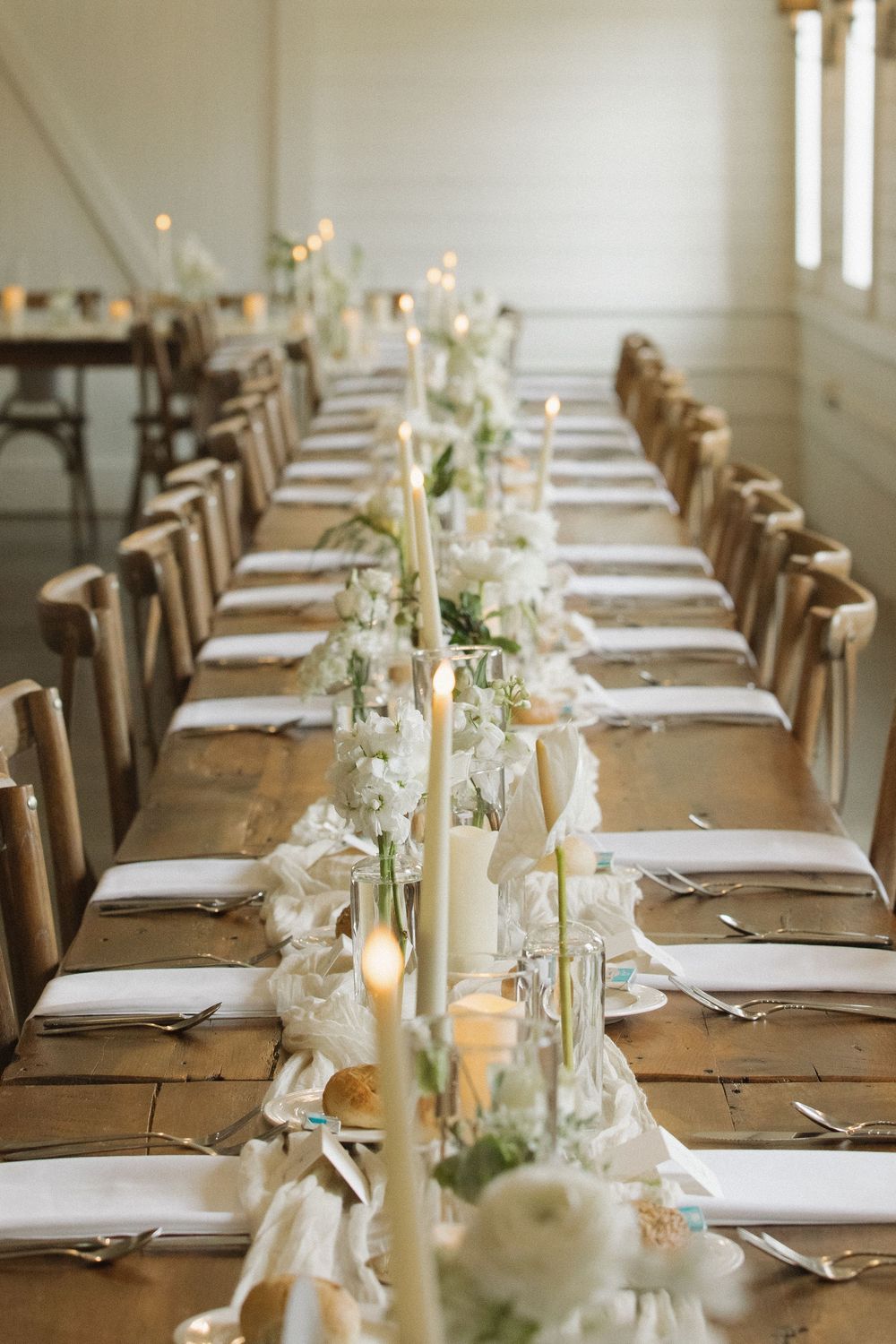 Long wooden farmhouse table set for wedding reception with white linens and elegant place settings.