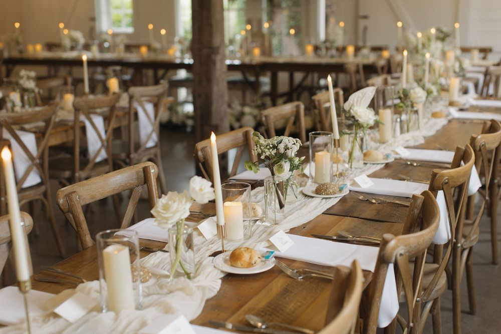 Elegant wedding reception table setting with wooden chairs, white linens, and delicate floral centerpieces.