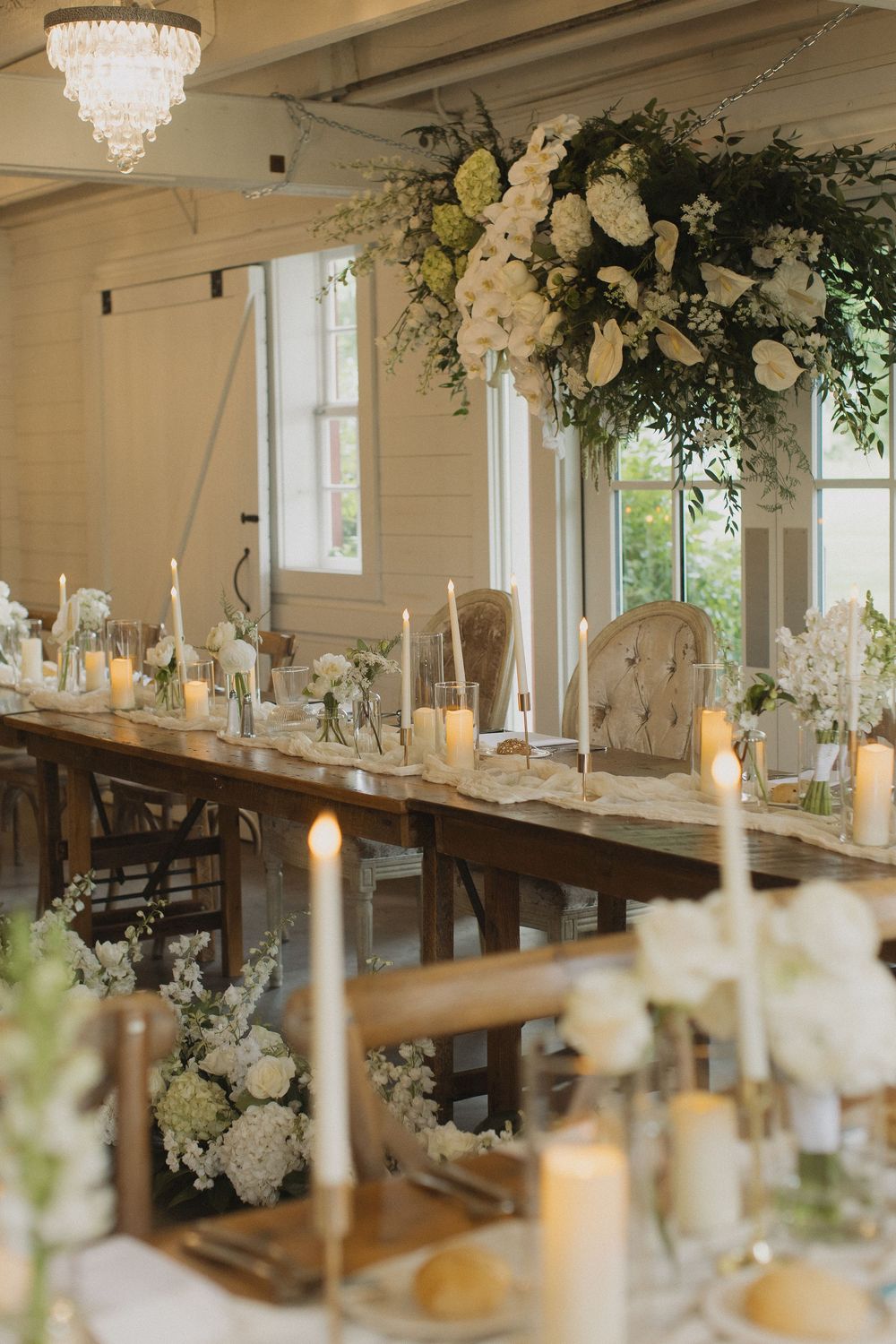 Wedding reception tables decorated with white floral arrangements and candlelight under crystal chandeliers.