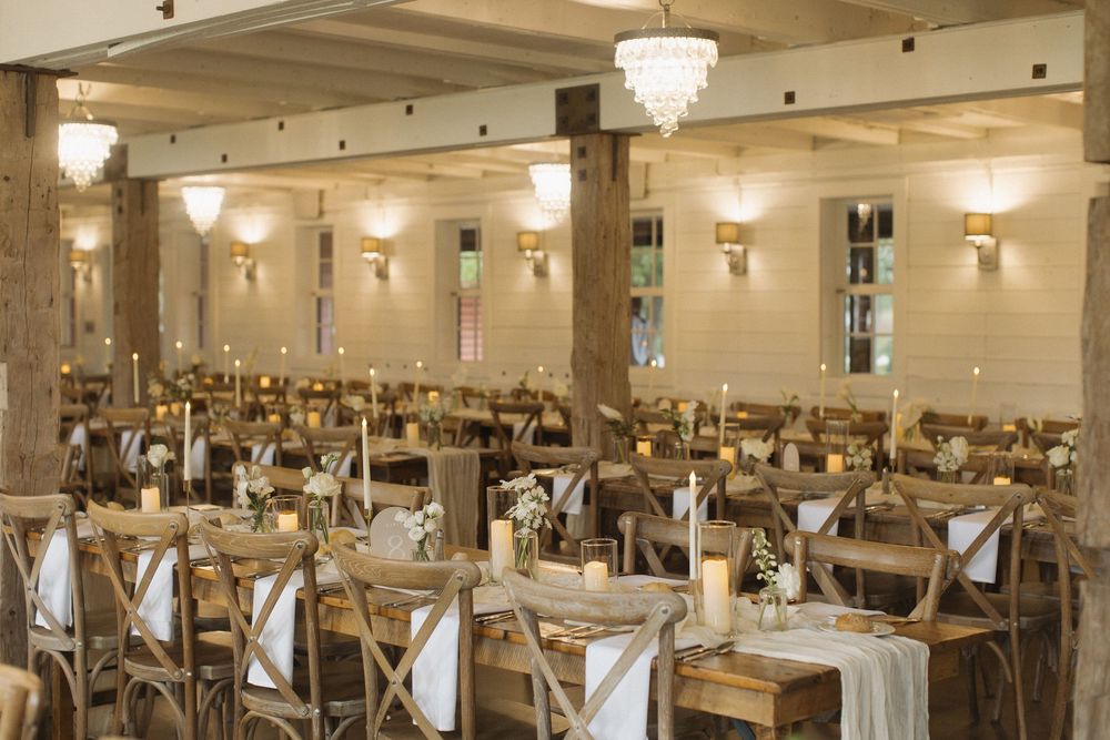 Spacious wedding venue with elegant table settings, chandeliers, and wall sconces creating warm ambiance.