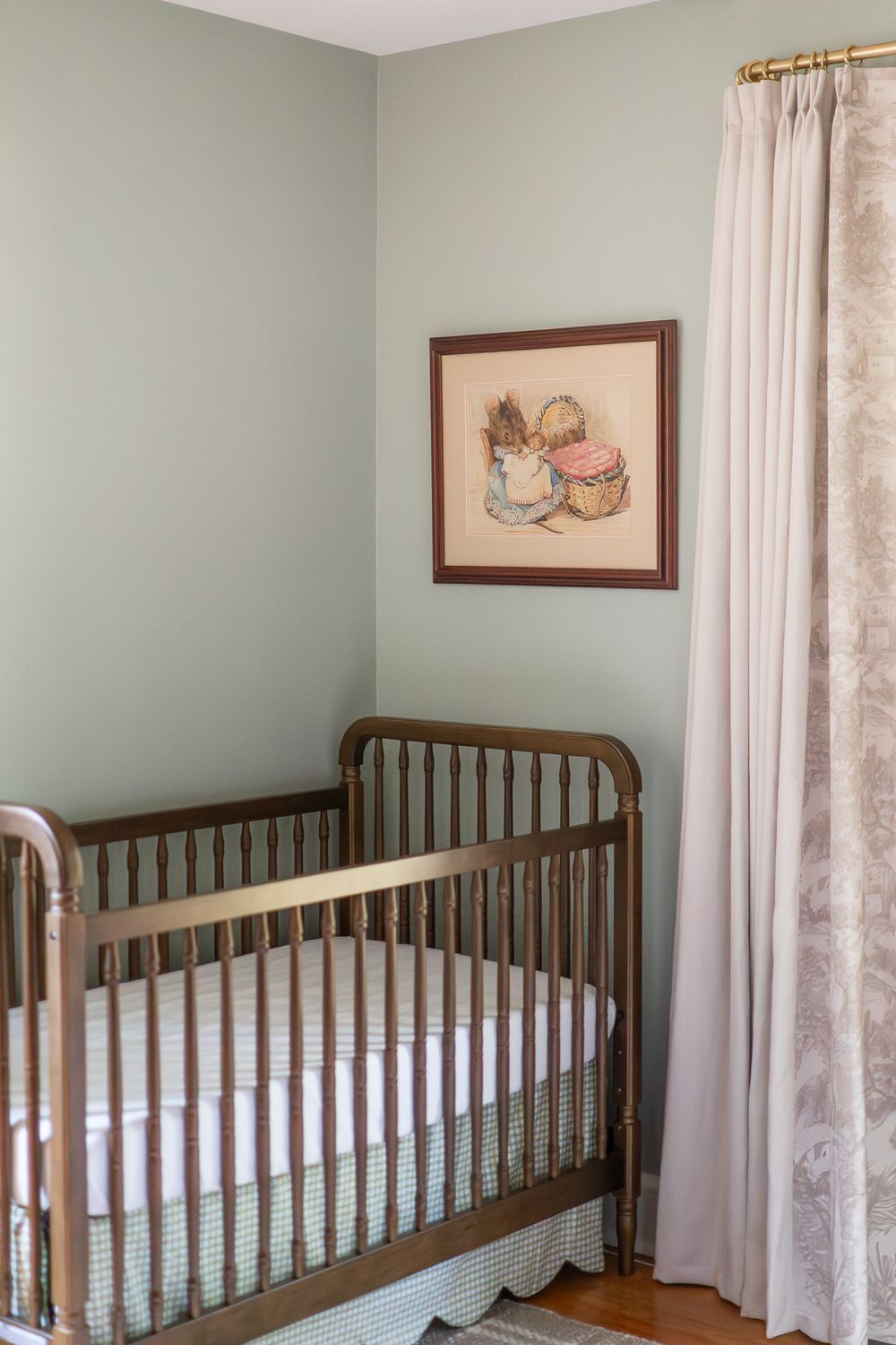 Panoramic view of a nursery room with wooden cribs against sage green walls and white lace curtains.