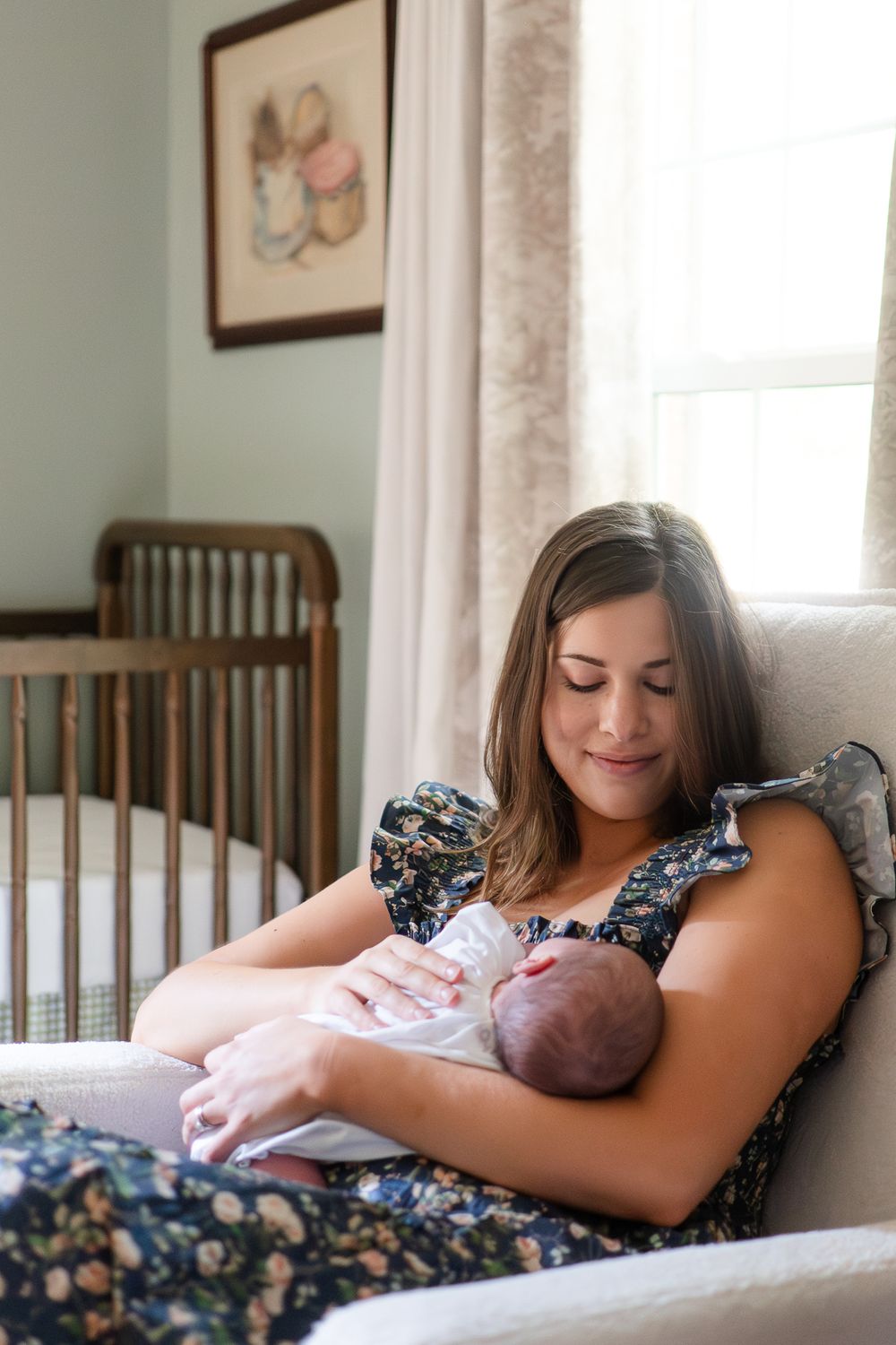 A tender moment as someone holds and gazes at a sleeping newborn baby in a cozy nursery with wooden crib and framed art.