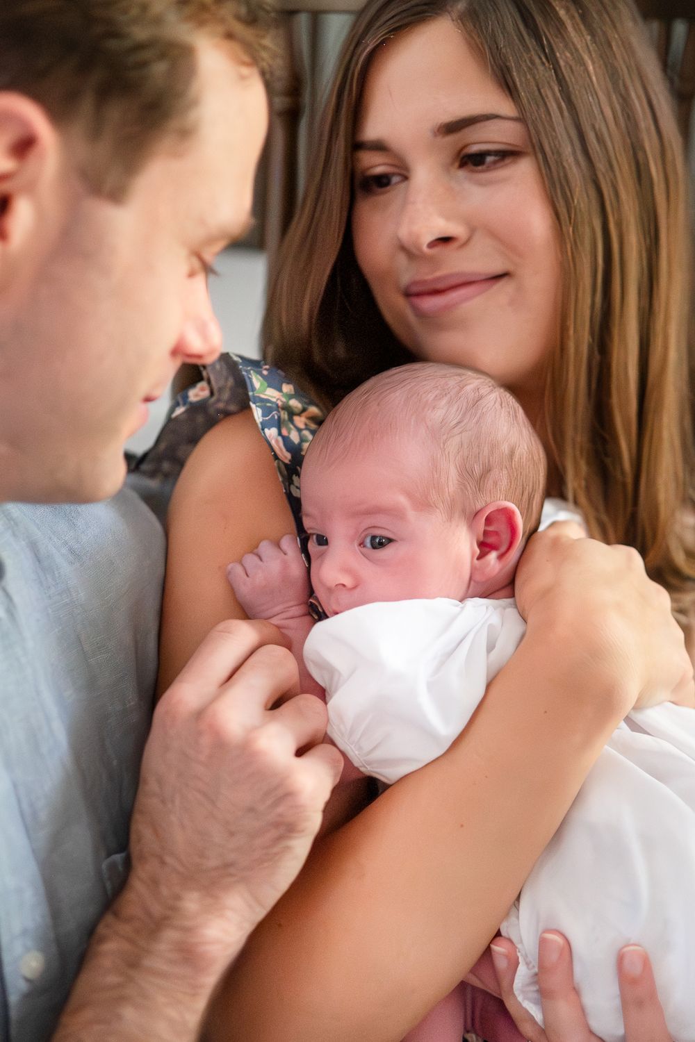 A couple gazes lovingly at their newborn baby wrapped in white, sharing an intimate family moment together.