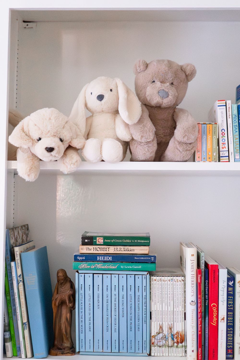 A row of plush teddy bears line a bookshelf above neatly arranged blue and multicolored books.