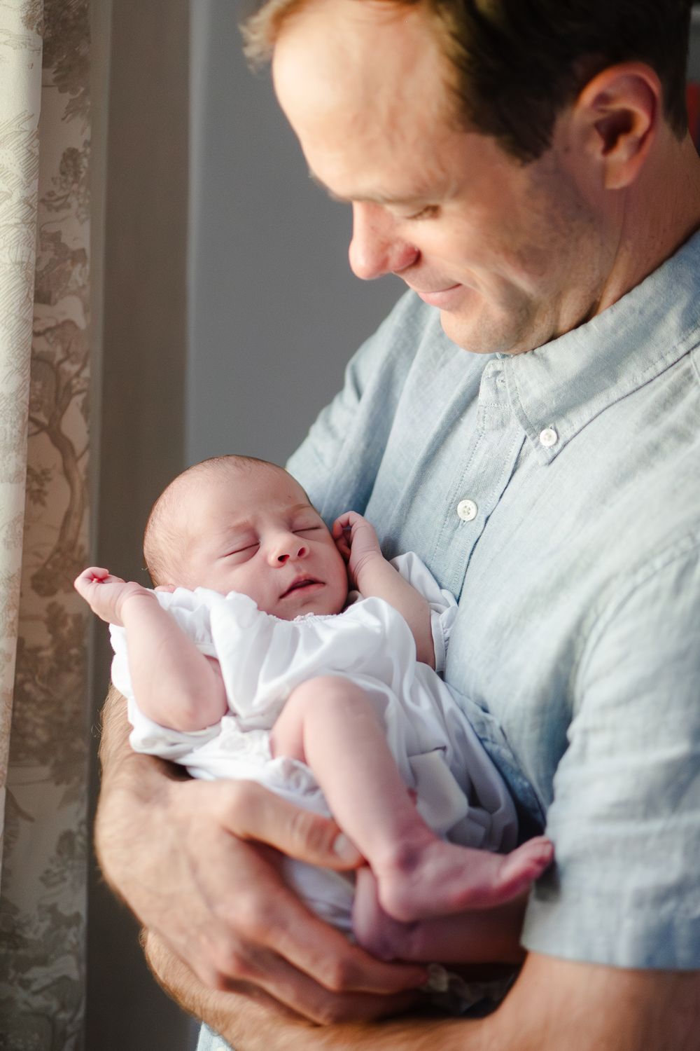 A parent in pale blue shirt cradles a sleeping newborn baby wearing white clothing in multiple tender moments.