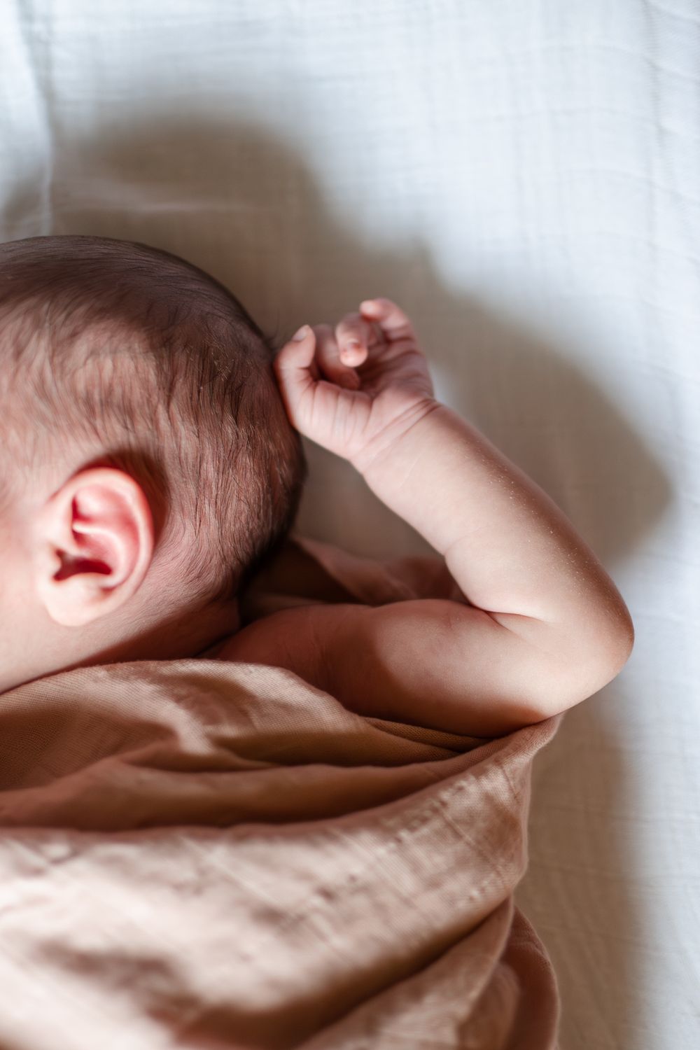 Baby wrapped in soft brown blanket resting on white bedding, shown from multiple angles in closeup shots.