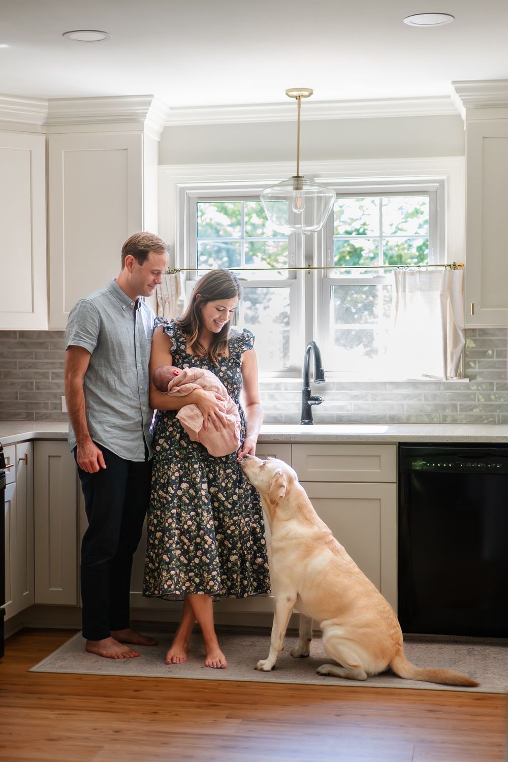 Couple and their yellow Labrador interact and smile together in their modern white kitchen with tile backsplash.